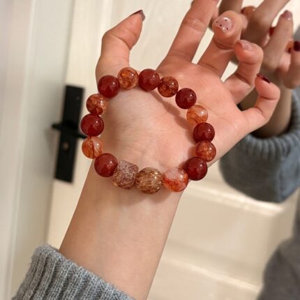 A woman wearing the natural red hematoid quartz and red agate beaded bracelet on her wrist, showcasing the gemstone patterns and square crystal cube.