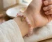 Minimalist rose quartz self compassion bracelet worn on a wrist, featuring faceted pink crystal beads, gold spacers, and a delicate heart-shaped dangling charm with a crystal center.